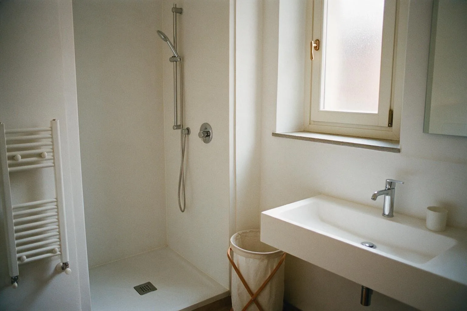 Un bagno rinnovato con doccia a filo pavimento, lavabo sospeso e finestra con vetro satinato