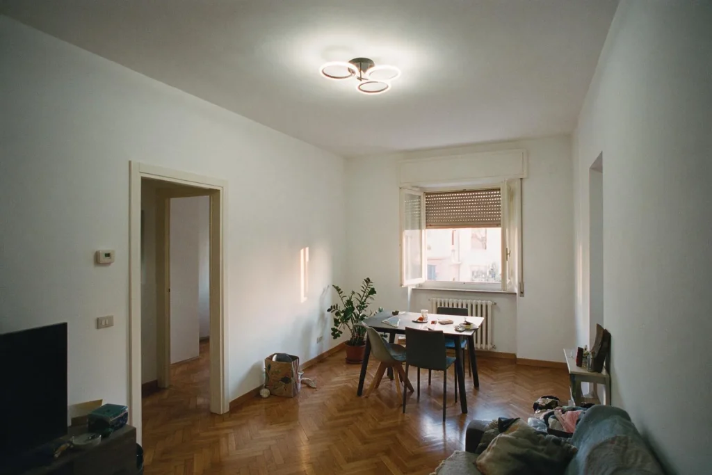 Un soggiorno con tavolo da pranzo, pavimento a spina di pesce, lampada a soffitto e una porta aperta sul corridoio