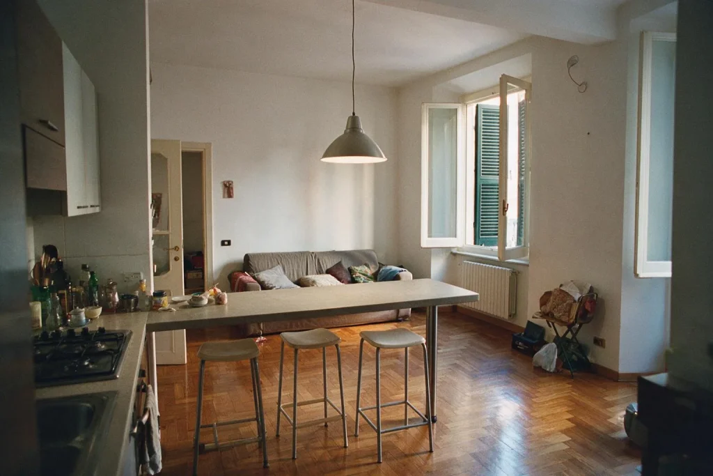 Una cucina aperta sul soggiorno con penisola, tre sgabelli, lampada a sospensione e un divano sullo sfondo