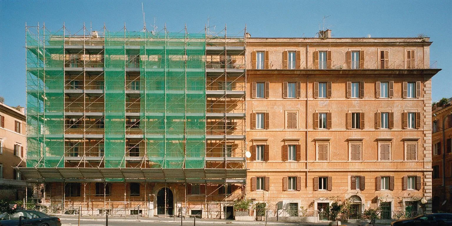 Facciata ocra di un palazzo romano di cinque piani con il ponteggio e la rete verde su metà del fronte
