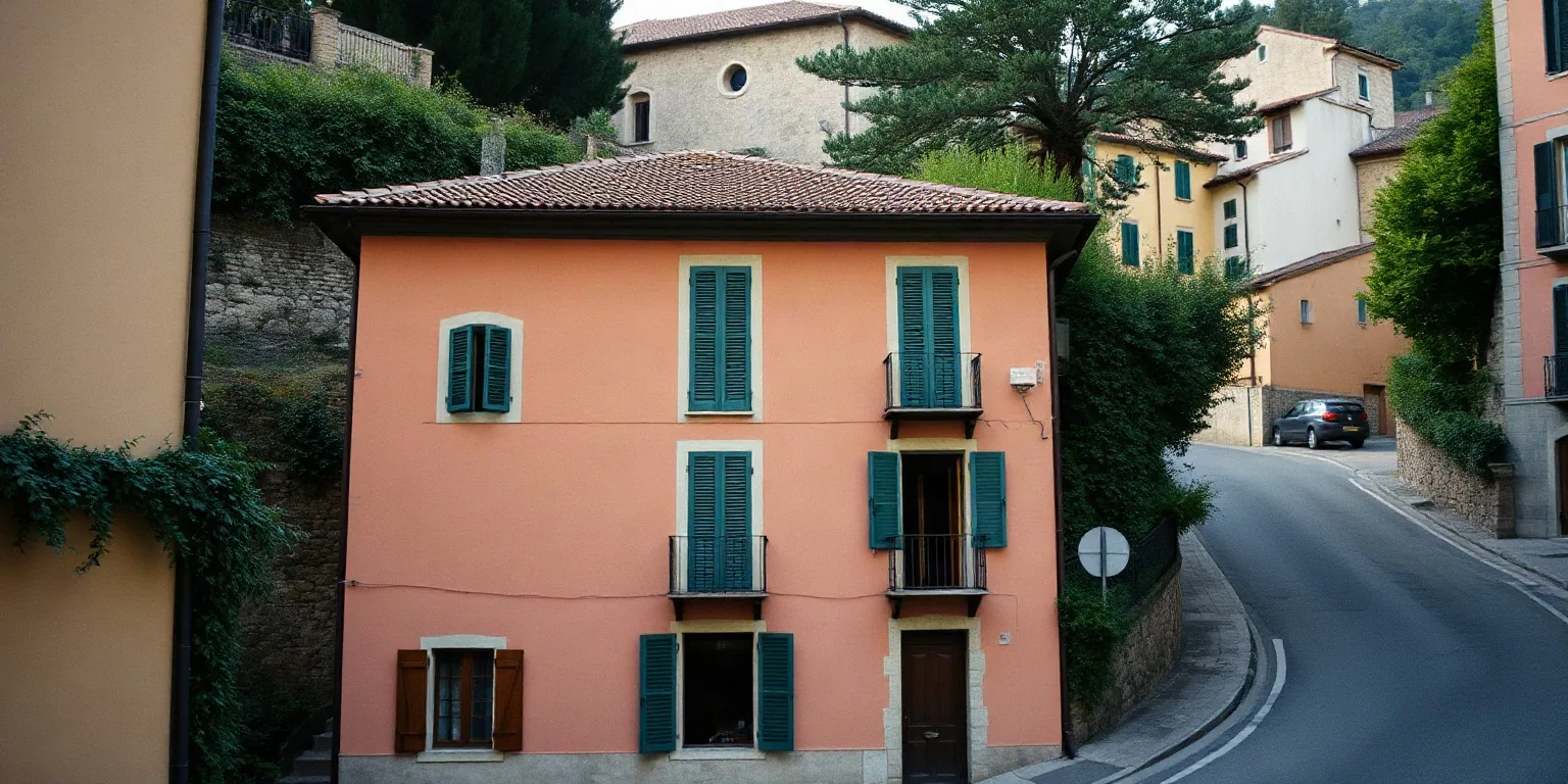 Una palazzina color pesca con le persiane verdi su una strada in salita