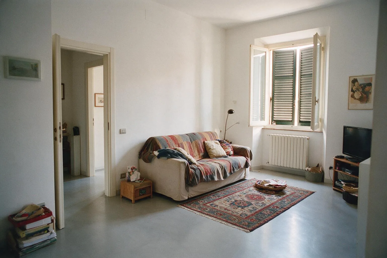 Un soggiorno con pavimento in resina grigio chiaro senza fughe, un divano con coperta colorata e un tappeto